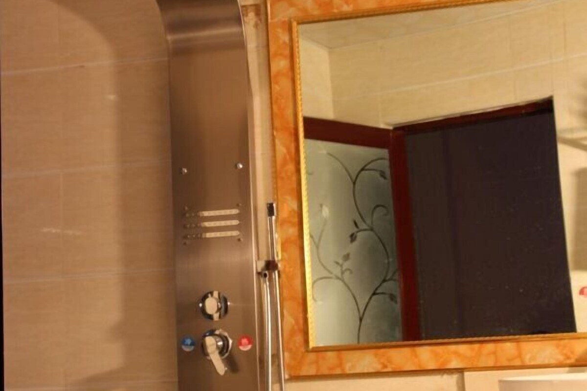 Uma casa de banho com parede de mármore, um espelho com moldura decorativa e zona de duche.