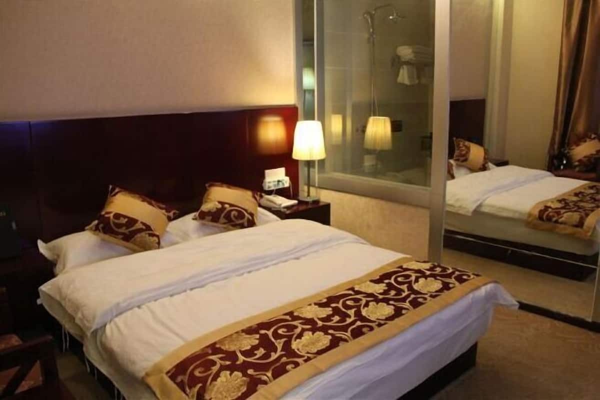 A hotel room with a bed, a nightstand with a lamp, a mirror, and a shower area.