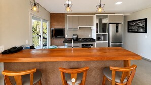 A modern kitchen with a central island, bar stools, and pendant lighting. - Paraíso do Coral - Vista Mar - Garopaba (Paulo Lopes)