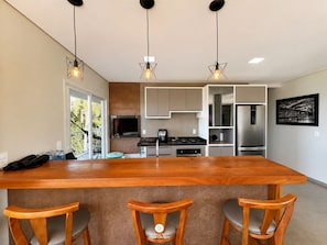 A modern kitchen with a central island, bar stools, and pendant lighting. - Paraíso do Coral - Vista Mar - Garopaba (Paulo Lopes)