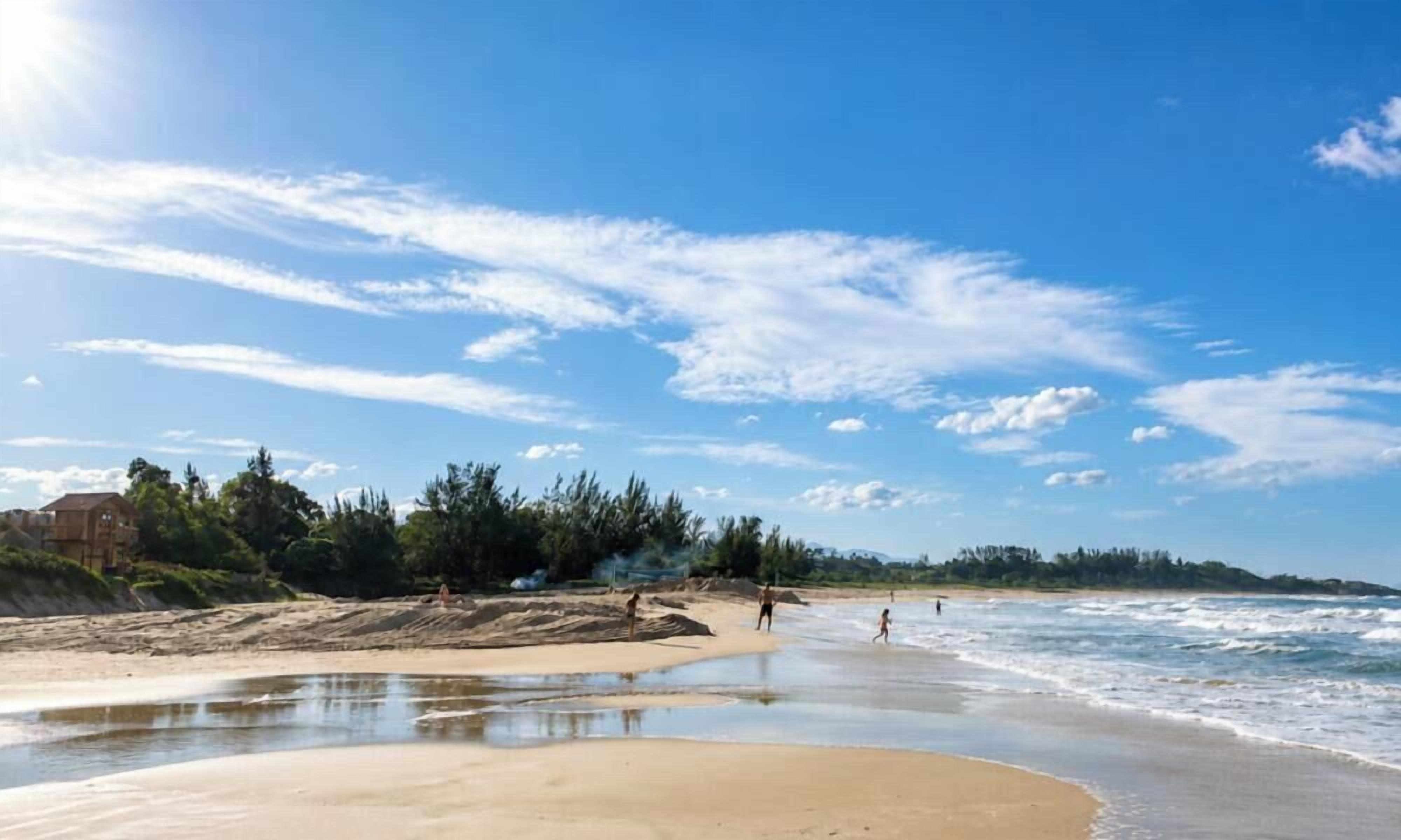 Uma praia com céu limpo, águas calmas e algumas pessoas.