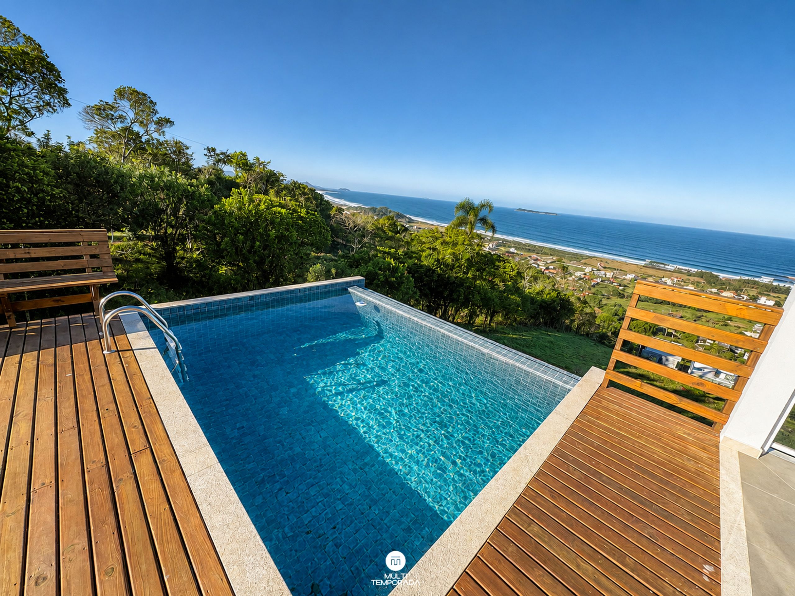 Piscina com deck de madeira e vista para o oceano.