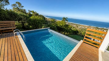 Piscina com deck de madeira e vista para o oceano.