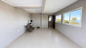 A spacious room with a tiled floor, a motorcycle parked against the wall, and a door leading to a bathroom. - Paraíso do Coral - Vista Mar - Garopaba (Paulo Lopes)