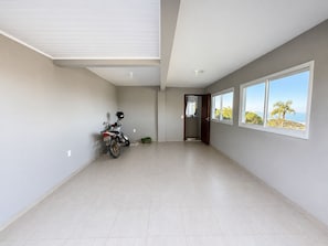 A spacious room with a tiled floor, a motorcycle parked against the wall, and a door leading to a bathroom. - Paraíso do Coral - Vista Mar - Garopaba (Paulo Lopes)