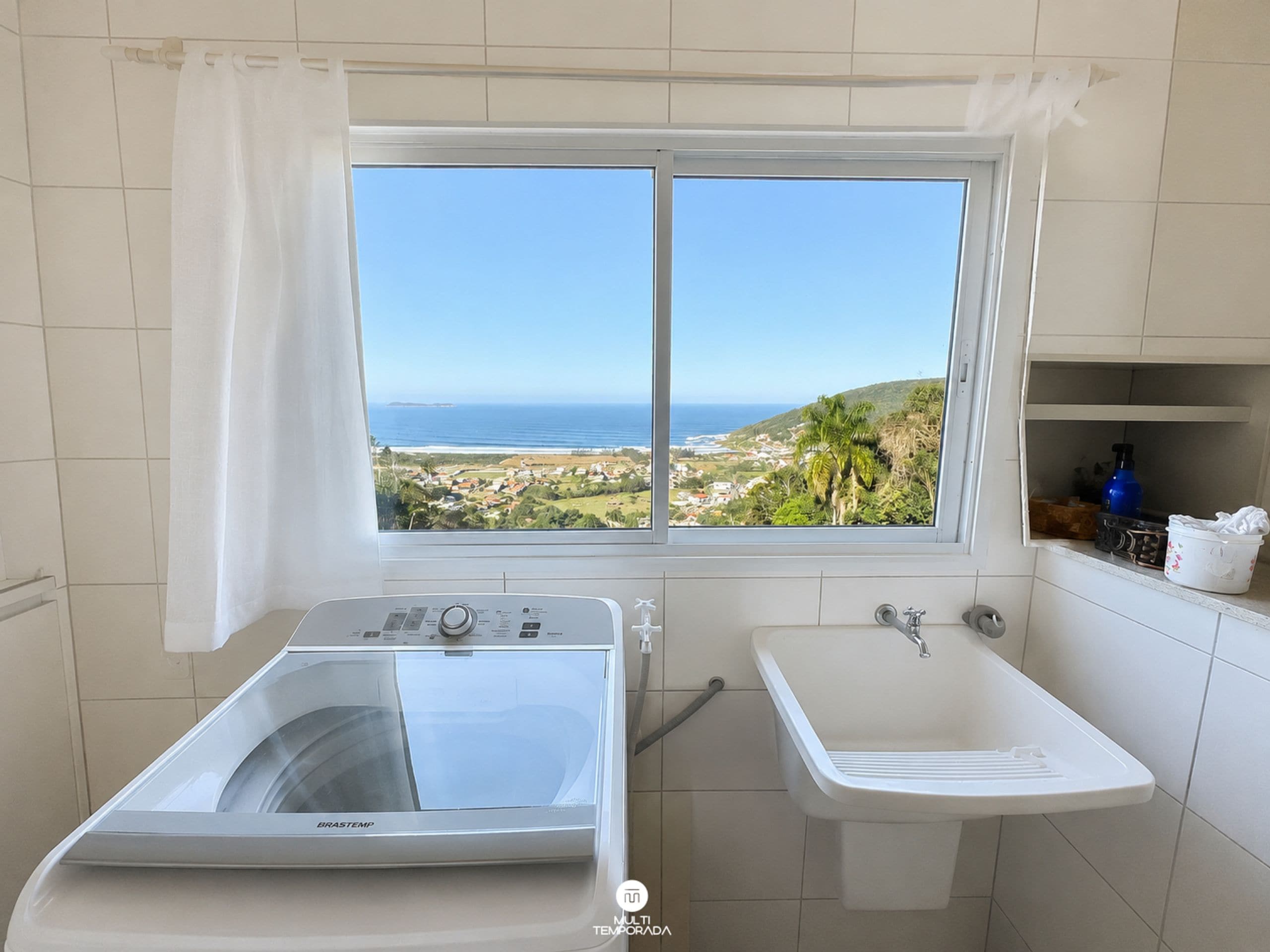 Casa de banho com vista para a paisagem costeira, máquina de lavar e lavatório.