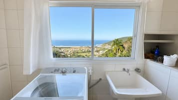 Casa de banho com vista para a paisagem costeira, máquina de lavar e lavatório.