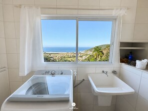 Un bagno con vista su un paesaggio costiero, una lavatrice e un lavandino.