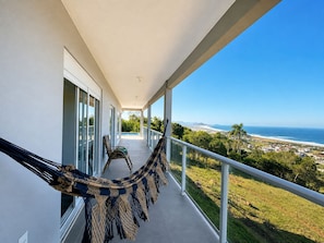 A balcony with a hammock, a view of the ocean, and a clear sky. - Paraíso do Coral - Vista Mar - Garopaba (Paulo Lopes)
