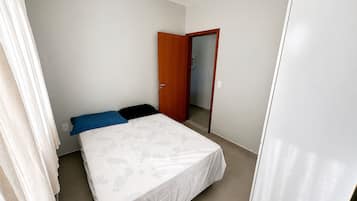 Um quarto com uma cama, uma porta e um guarda-roupa branco.