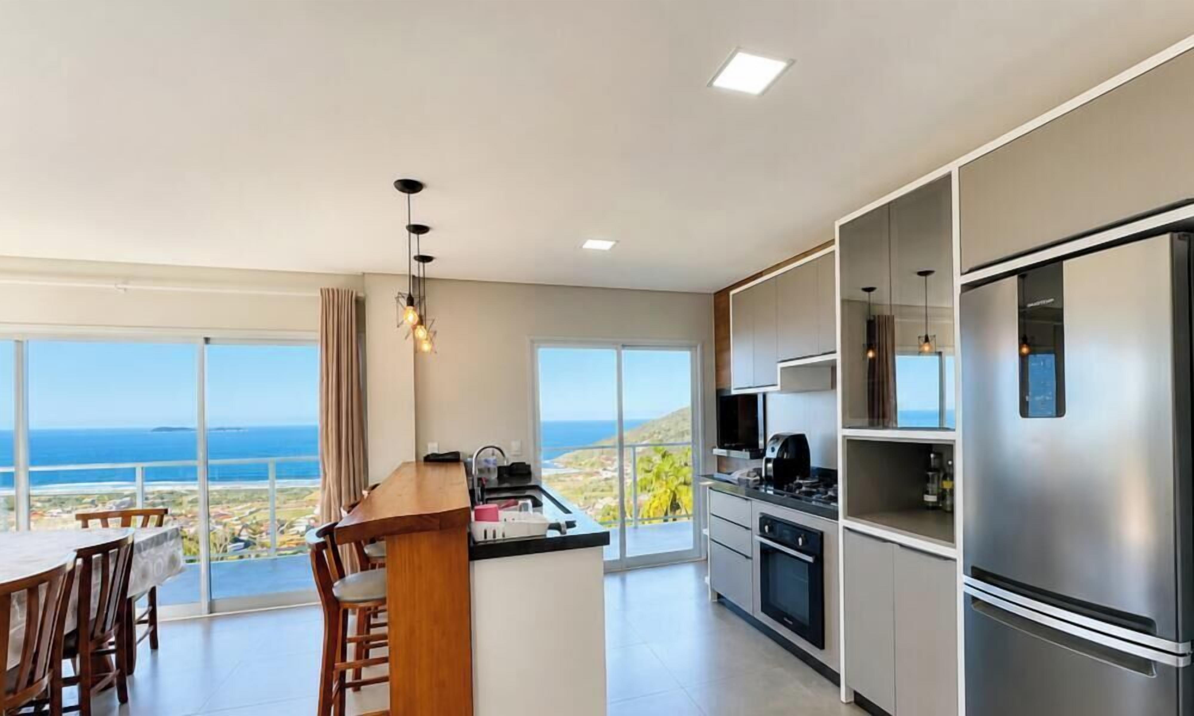 Cozinha moderna com uma ilha grande, eletrodomésticos de aço inoxidável e vista para o oceano.