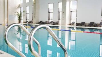 A swimming pool with metal handrails, lounge chairs, and large windows in the background.