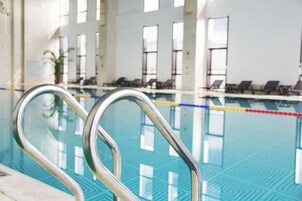 Una piscina con barandales metálicos, sillas de descanso y grandes ventanales al fondo.