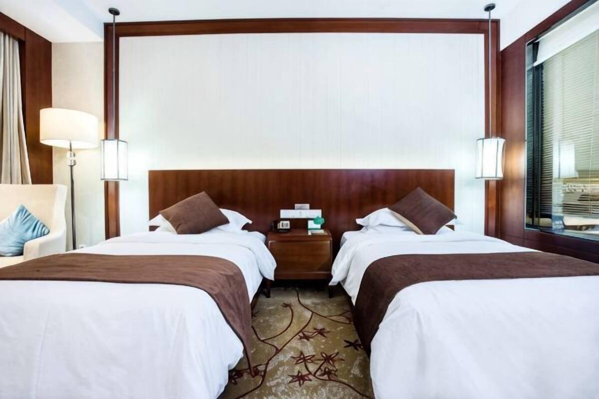 Hotellihuone, jossa on kaksi sänkyä, yöpöytä, lamppu ja ikkuna, jossa on sälekaihtimet.