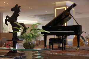 Un piano de cola, una mesa de vidrio con una planta y una estatua de un caballo en un vestíbulo.