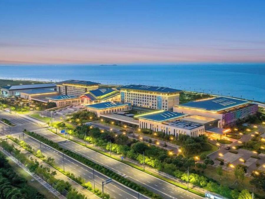 Un complex hoteler amb diversos edificis, una zona d'aparcament i vista al mar.