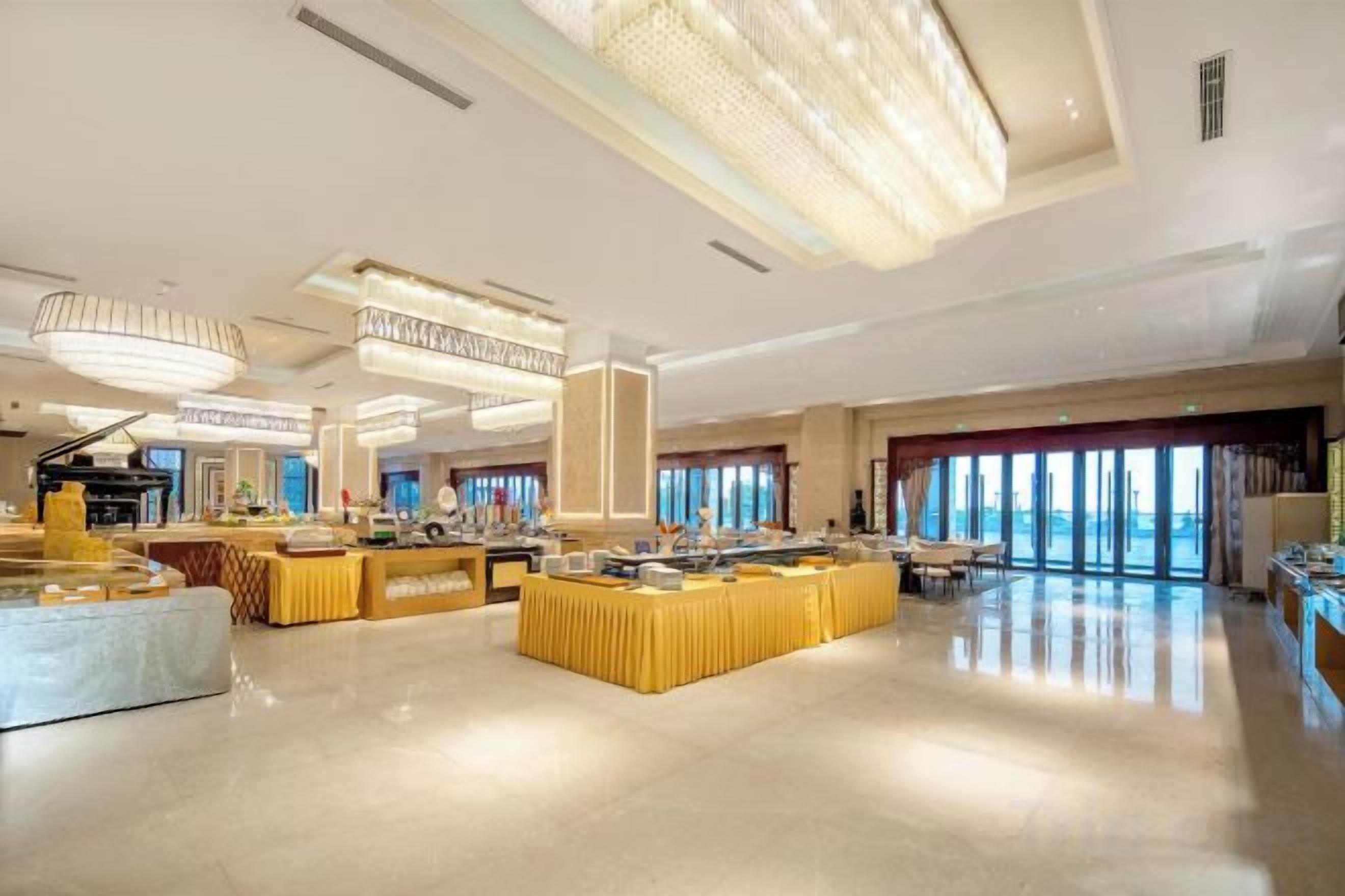 Een ruime hotellobby met een centraal buffetgedeelte, verschillende zithoeken en grote ramen die voor natuurlijk licht zorgen.