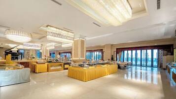Een ruime hotellobby met een centraal buffetgedeelte, verschillende zithoeken en grote ramen die voor natuurlijk licht zorgen.