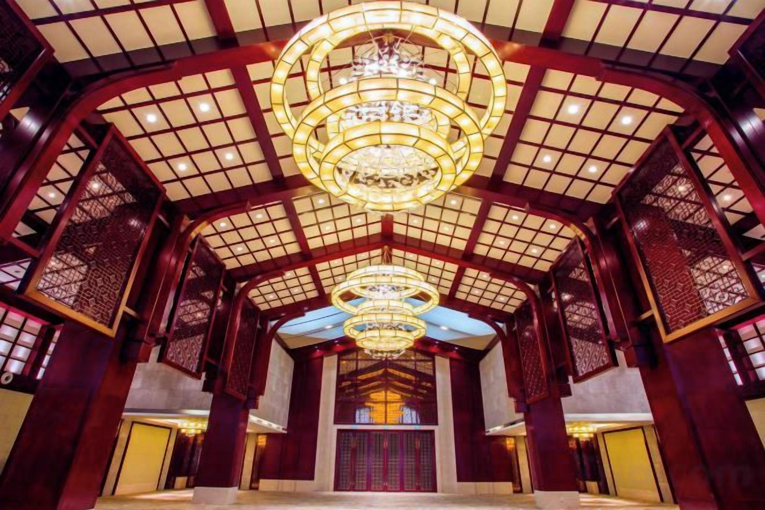 A traditional interior with a high ceiling, ornate wooden lattice, and a central chandelier.
