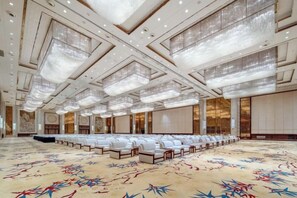 A spacious conference room with rows of white chairs, a patterned carpet, and a high ceiling with chandeliers. - Jinling Haizhou Bayview Conference Center (Lianyungang)
