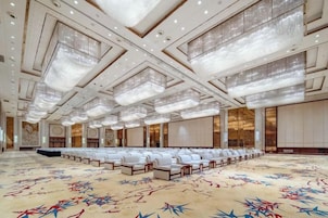 Una amplia sala de conferencias con filas de sillas blancas, una alfombra estampada y un techo alto con candelabros.