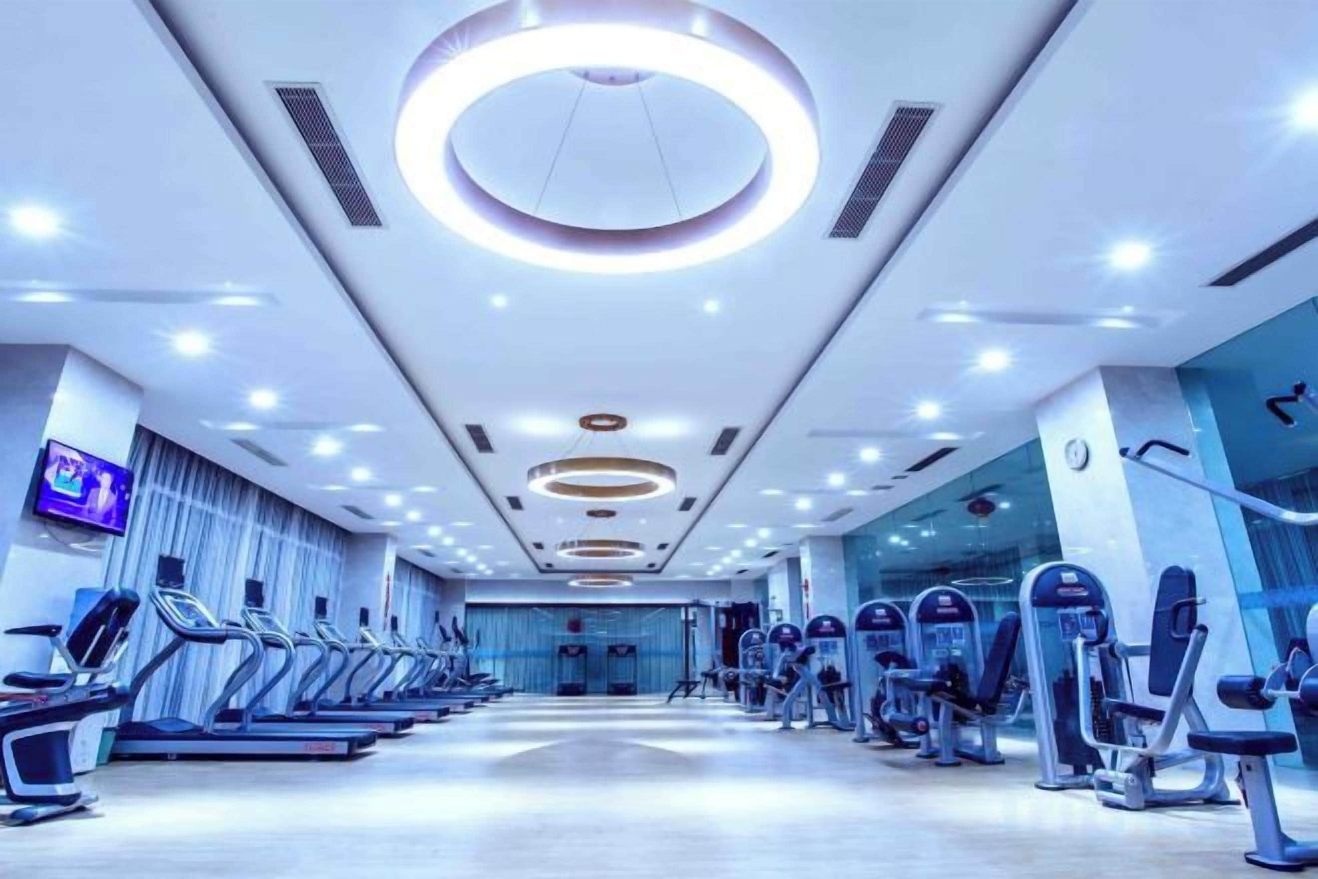 Ein Fitnessstudio mit Laufbändern, Crosstrainern und einem Fernseher an der Wand.