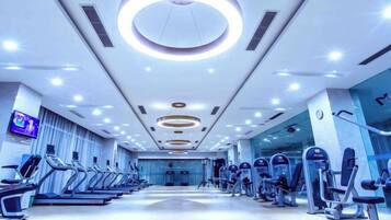 Ein Fitnessstudio mit Laufbändern, Crosstrainern und einem Fernseher an der Wand.
