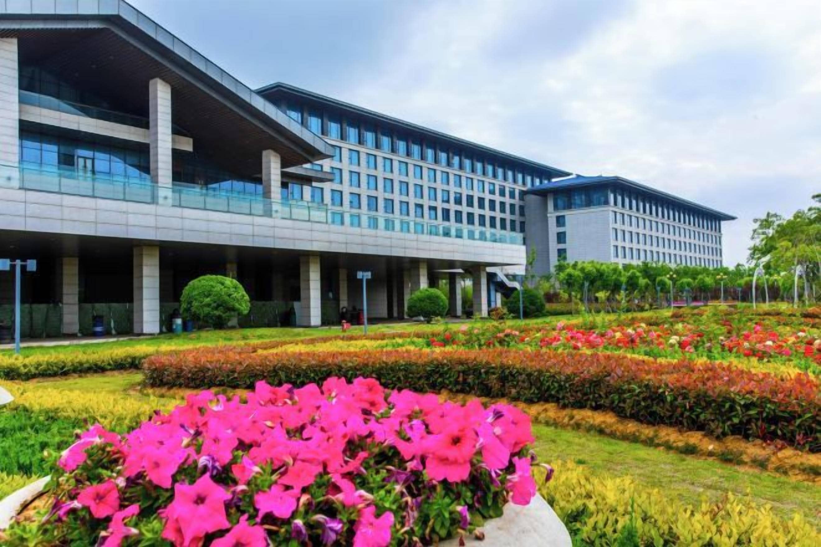 A modern building with a flat roof, large windows, and a landscaped garden with pink flowers.