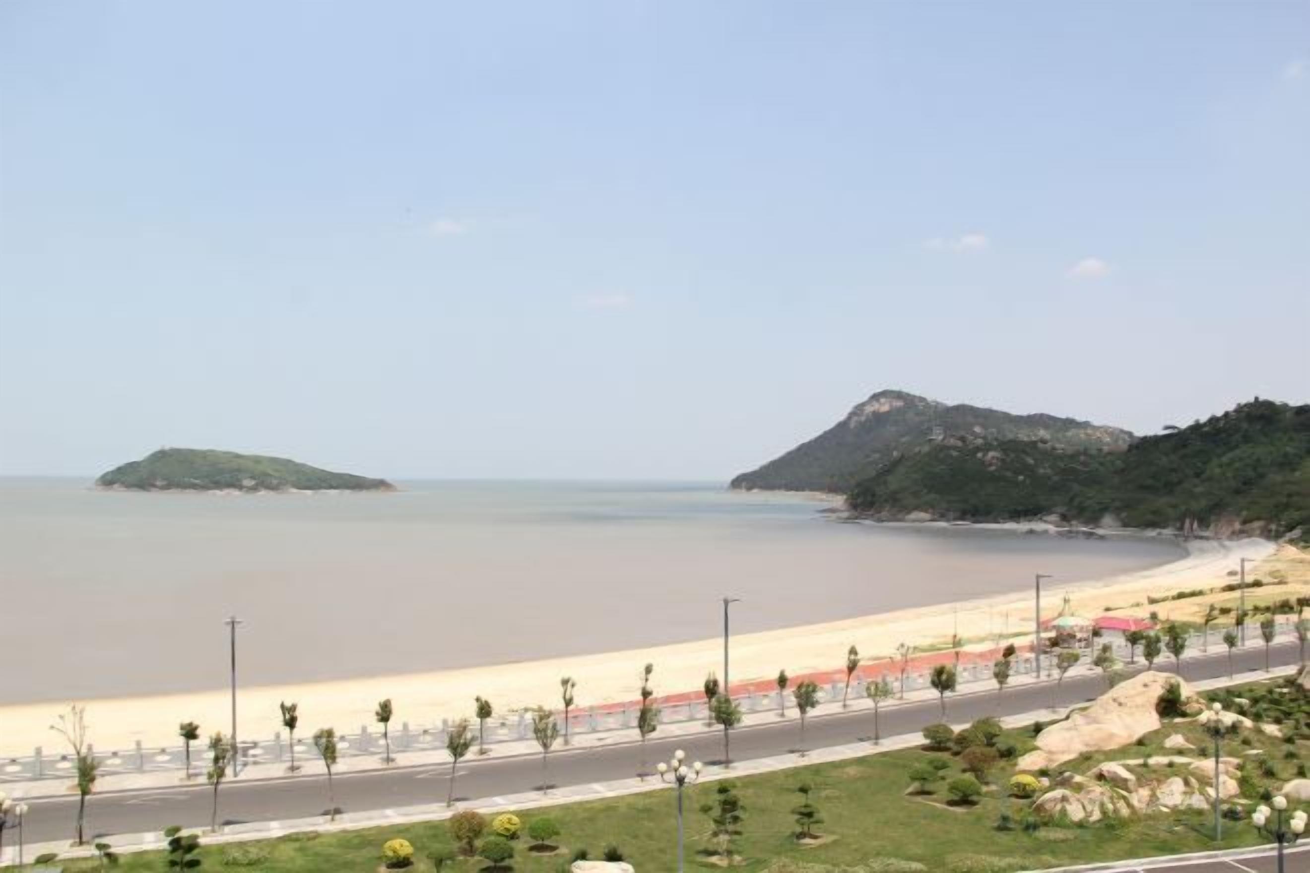 A coastal road with a beach and hills in the background.