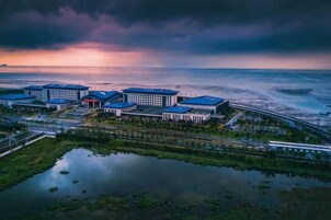 Complejo hotelero frente al mar con varias edificaciones, un puerto deportivo y una extensión de agua que refleja las estructuras.