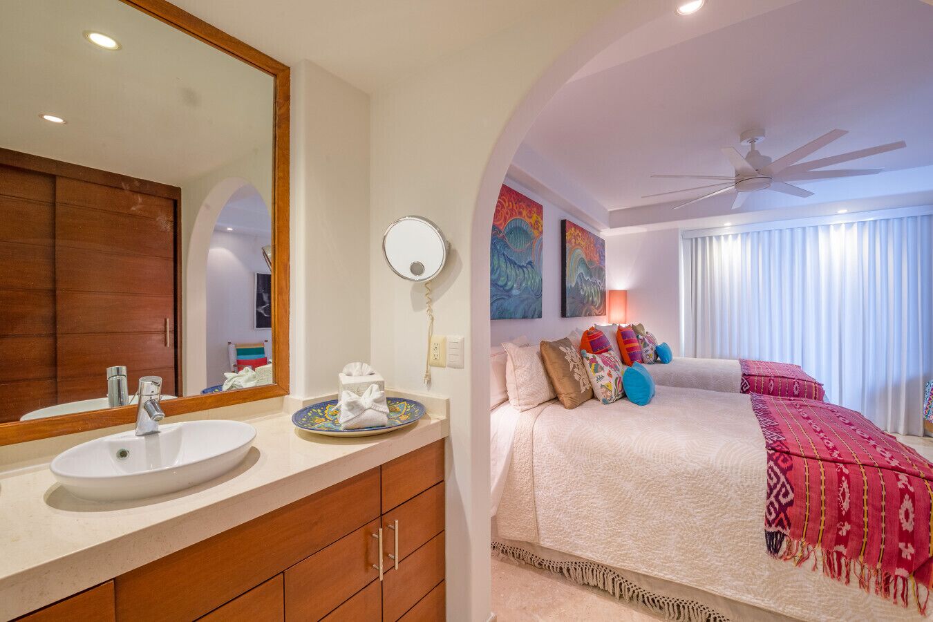 A modern hotel room with a large bed, a bathroom with a sink and mirror, and a ceiling fan.