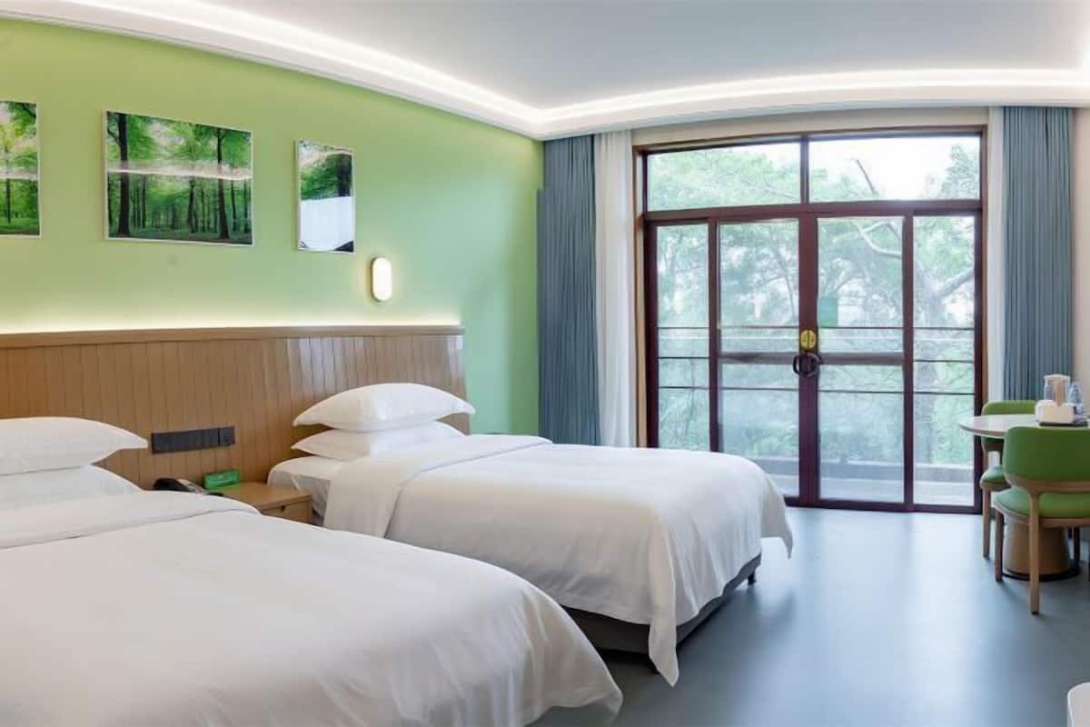 Una habitación de hotel con dos camas, un ventanal grande y una pequeña mesa con sillas.
