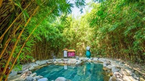 Una piscina cristalina rodeada de rocas y bambú, con una pequeña construcción al fondo.