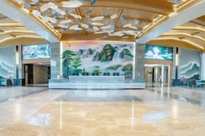 A spacious lobby with a large mural, a reception desk, and a modern ceiling design.