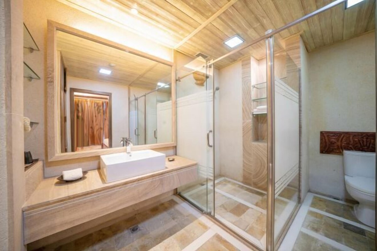 A modern bathroom with a wooden vanity, a large mirror, a glass shower enclosure, and a toilet.