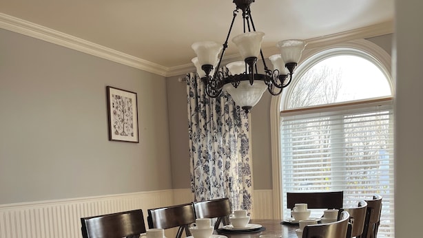 A dining room with a wooden table set for six, surrounded by dark wooden chairs. A chandelier hangs from the ceiling, and there is a window with blinds to the right. - Spacious - 3 bedrooms house in Granby, Quebec (Granby)