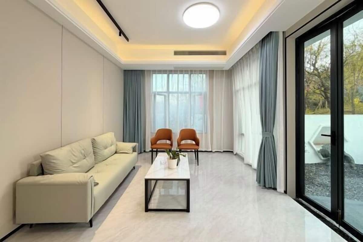 A modern living room with a sofa, two armchairs, a coffee table, and a large window with curtains.
