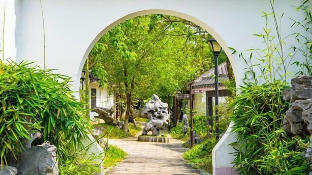 A pathway leading through an archway surrounded by lush greenery and a stone sculpture. - Stone Hotel (Yingde)
