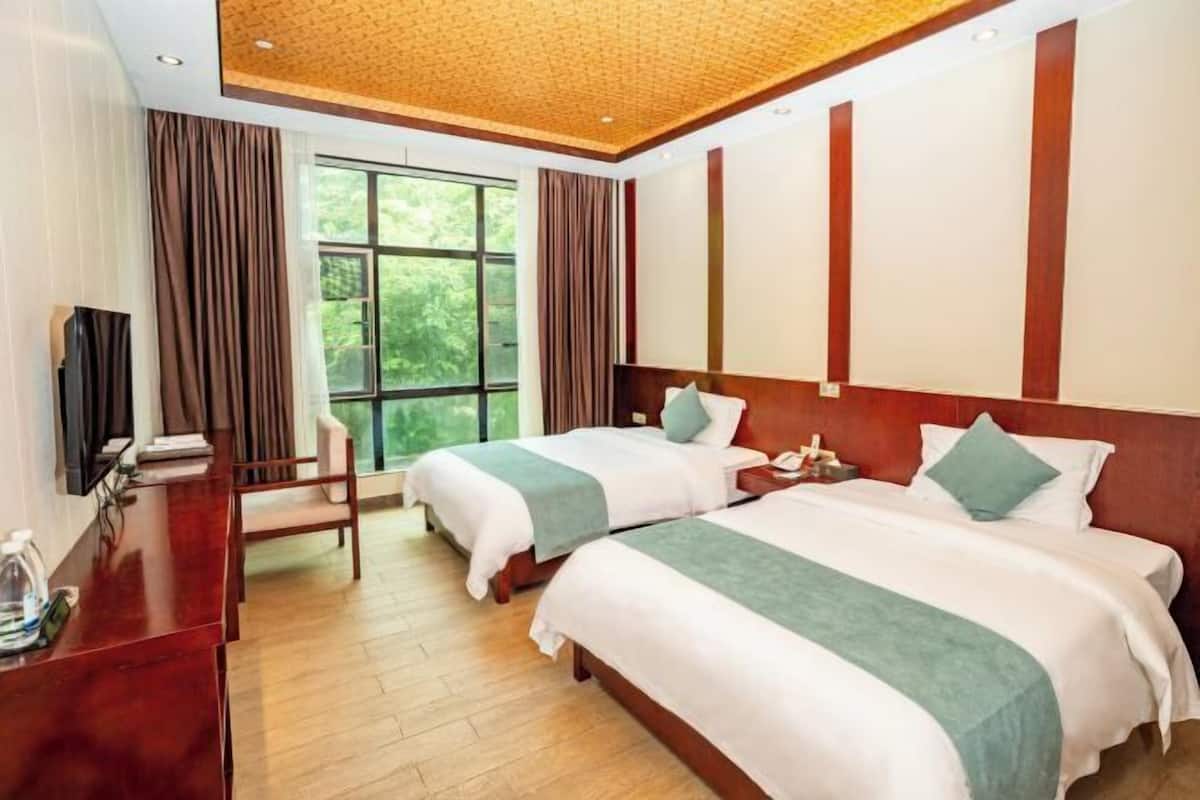 A hotel room with two beds, a desk, a TV, and a large window.