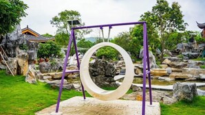 A garden with a circular stone structure, a traditional building, and a pond. - Stone Hotel (Yingde)
