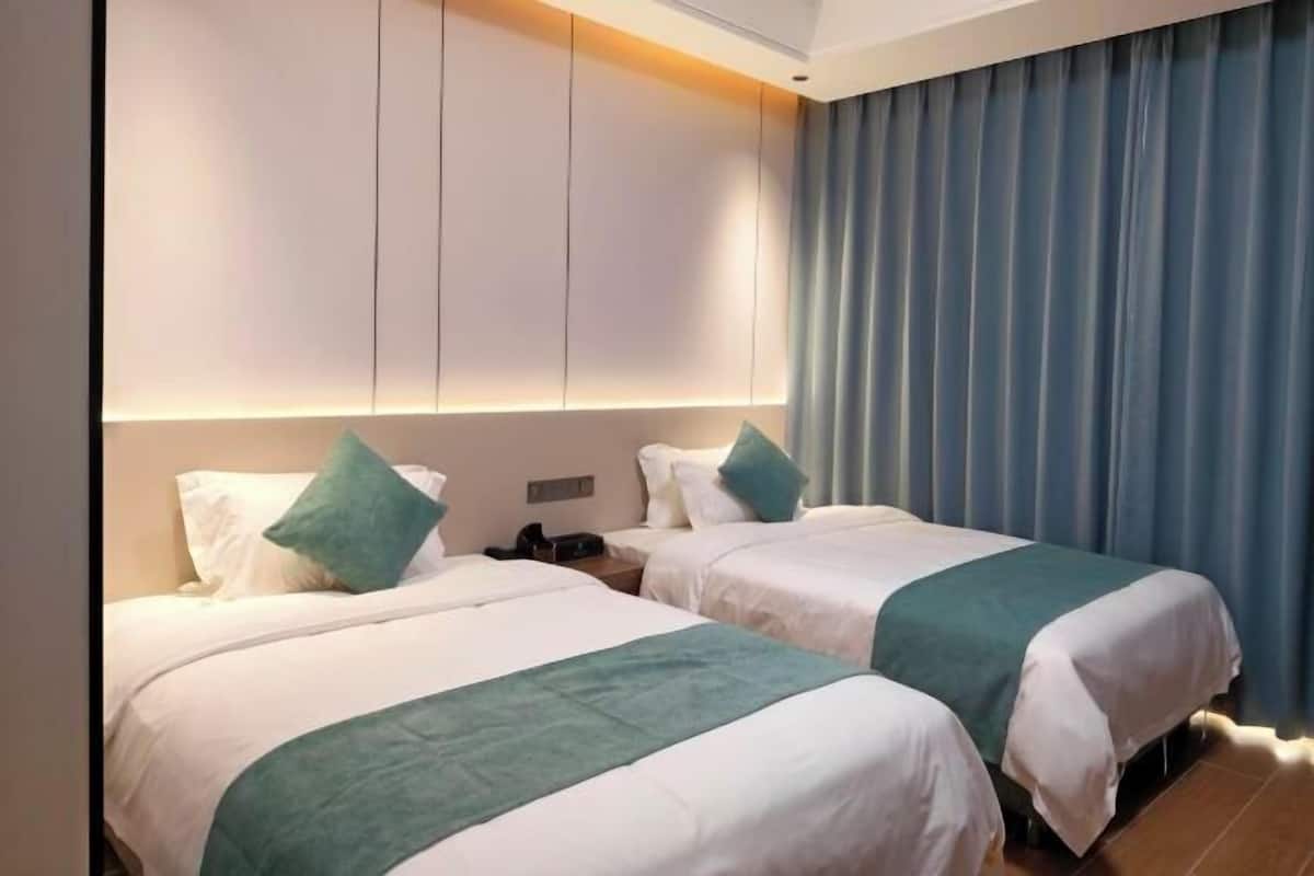 A hotel room with two beds, a headboard with integrated lighting, a telephone, and a curtain.