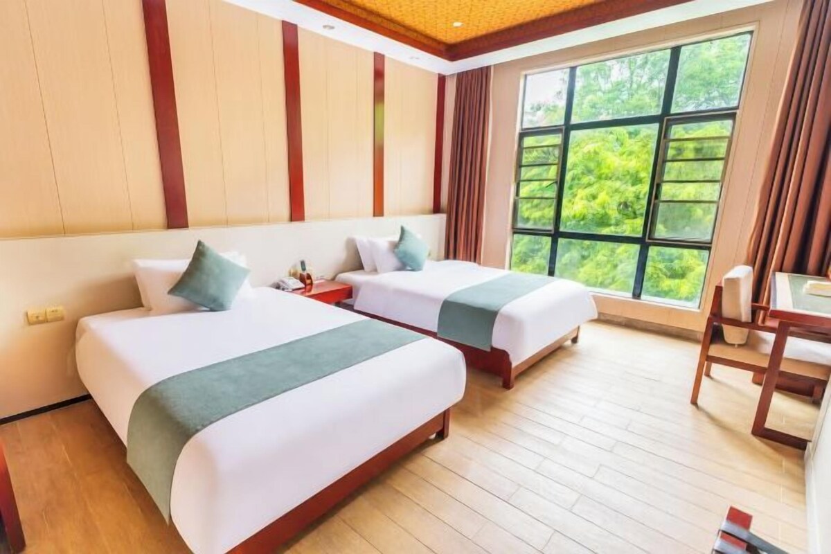 A hotel room with two beds, a wooden floor, a large window, and a dining area.