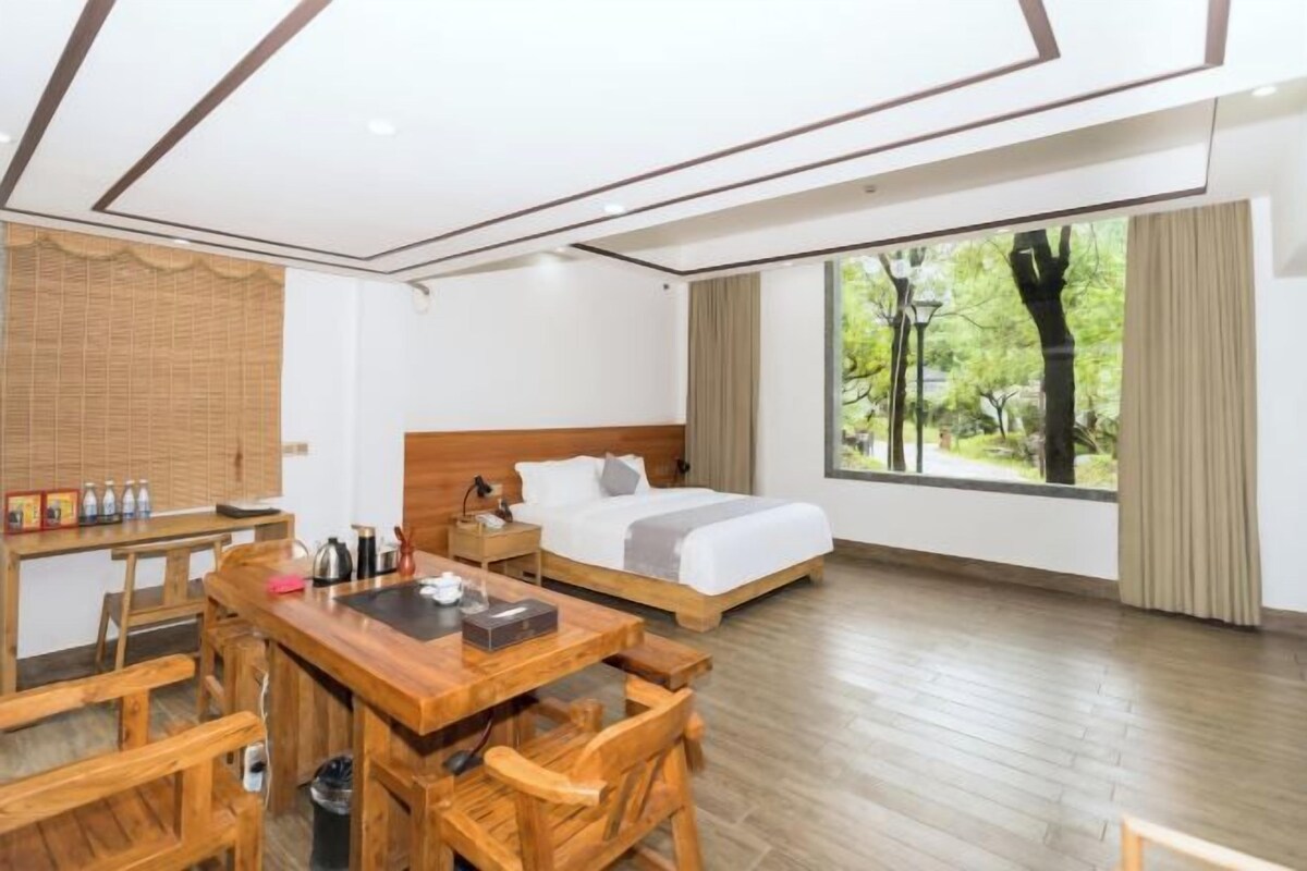 A hotel room with a bed, a desk, and a view of trees.