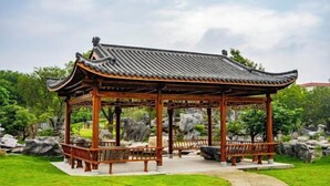 A traditional wooden pavilion with a tiled roof, surrounded by a well-maintained garden with rocks and greenery. - Stone Hotel (Yingde)