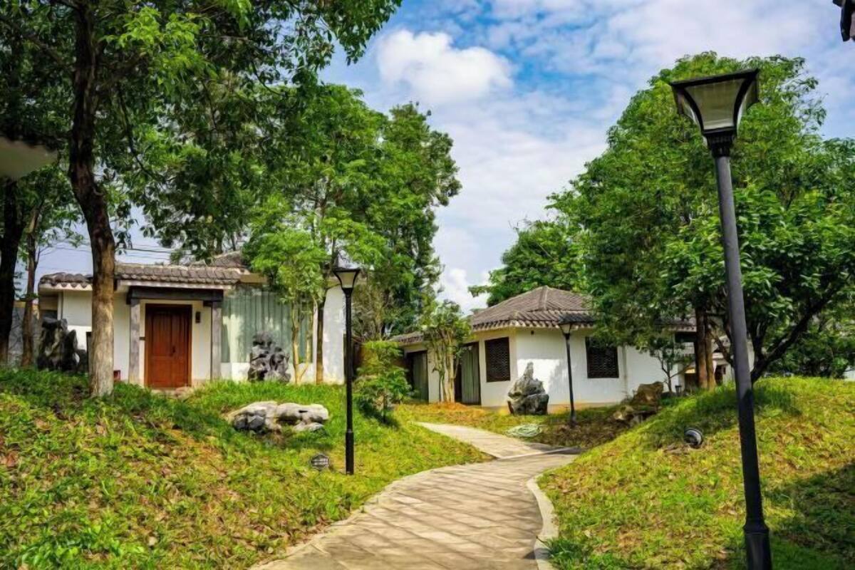 A pathway leading to a building with a tiled roof, surrounded by greenery and a street lamp.