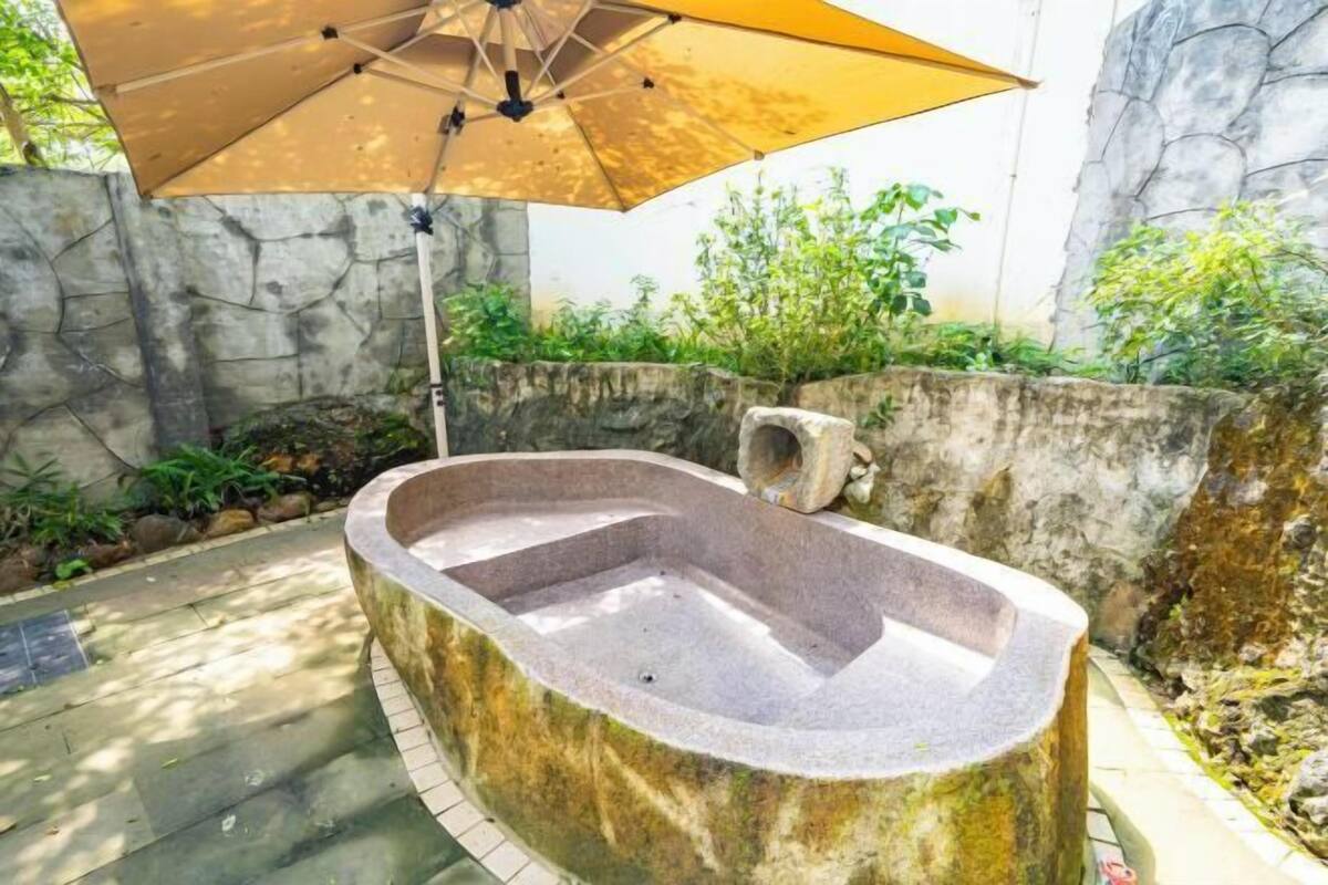 A stone hot tub with a wooden deck, surrounded by a stone wall and greenery.