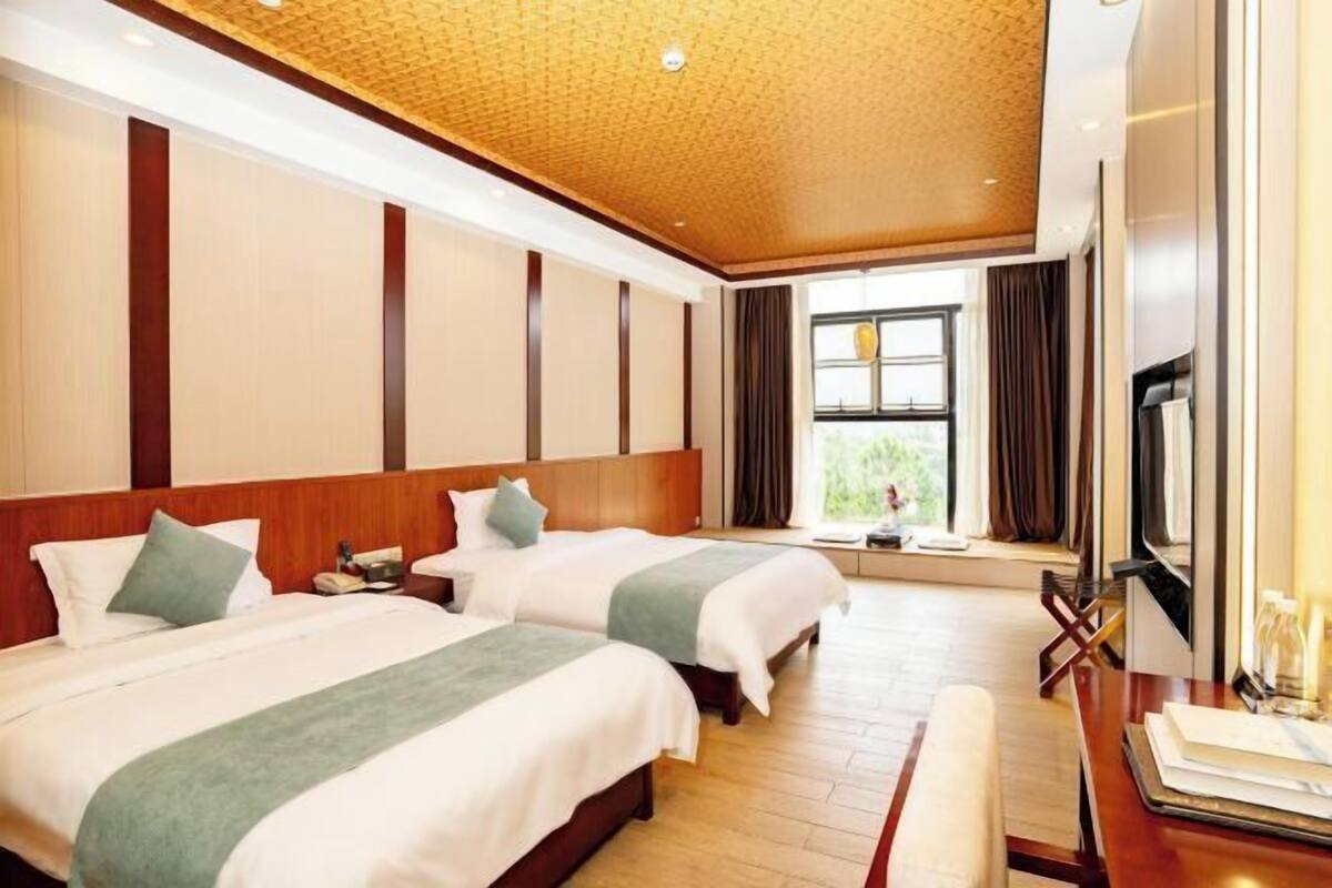 A hotel room with two beds, a wooden ceiling, a large window, and a flat-screen TV.