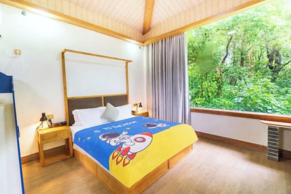 A bedroom with a bed, nightstands, a window with a forest view, and a ceiling with wooden beams.