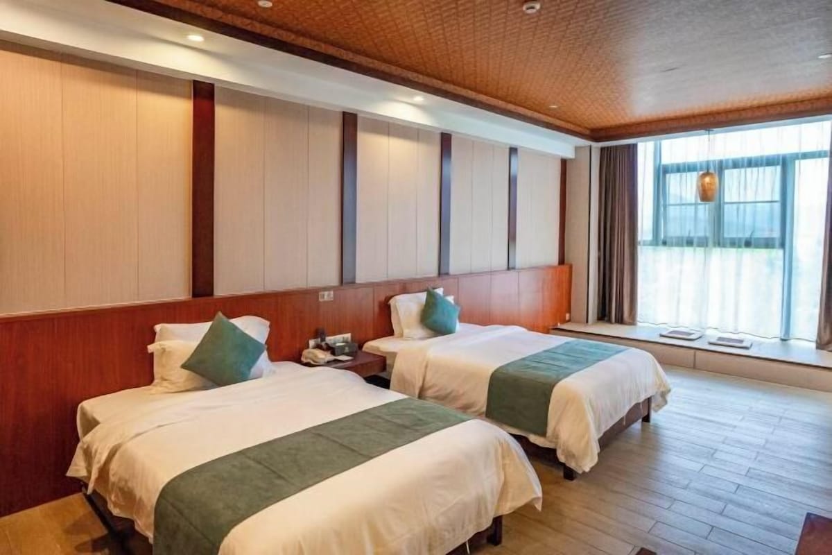 A hotel room with two beds, wooden paneling on the walls, a large window with curtains, and a wooden floor.