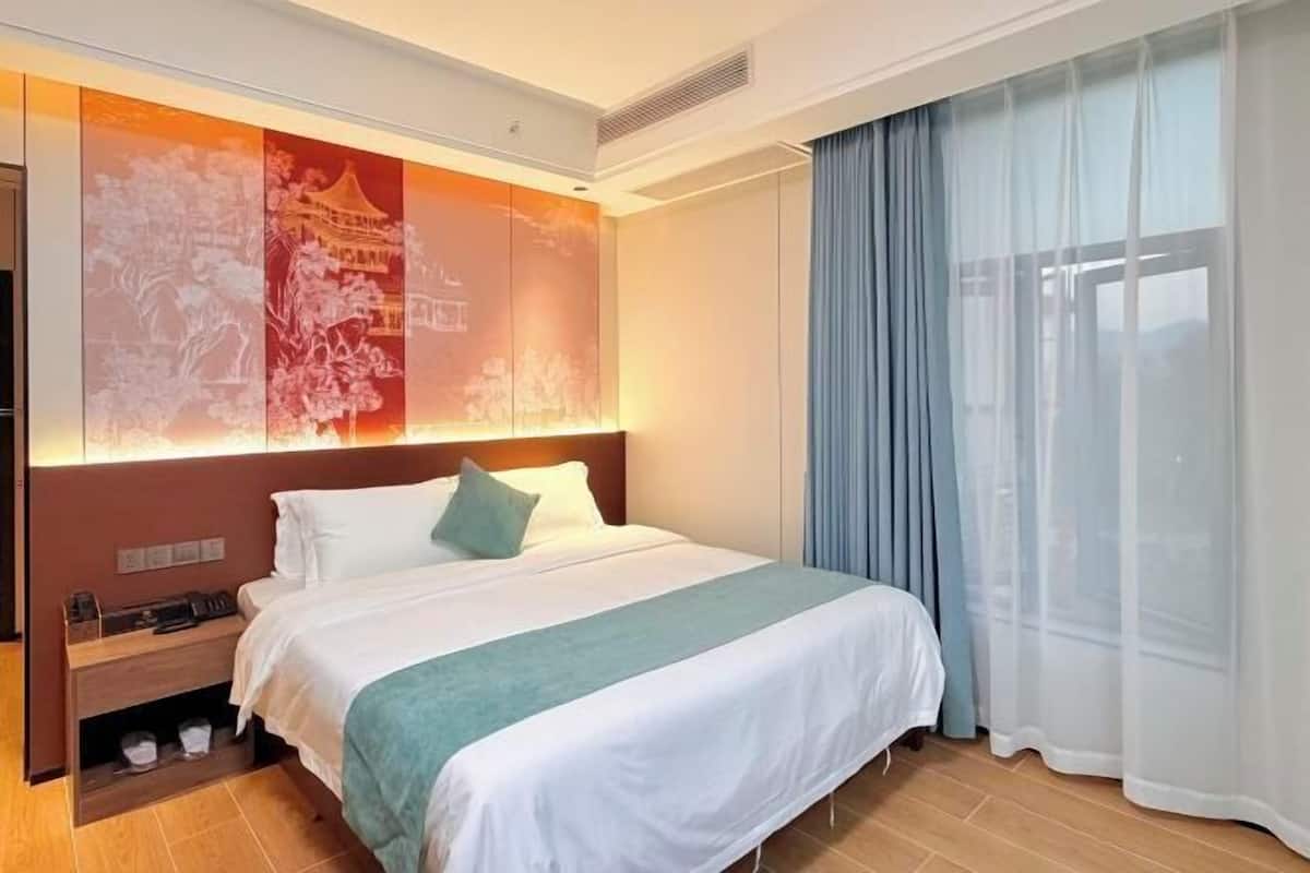 A hotel room with a large bed, a nightstand, a wall-mounted TV, and a window with curtains.